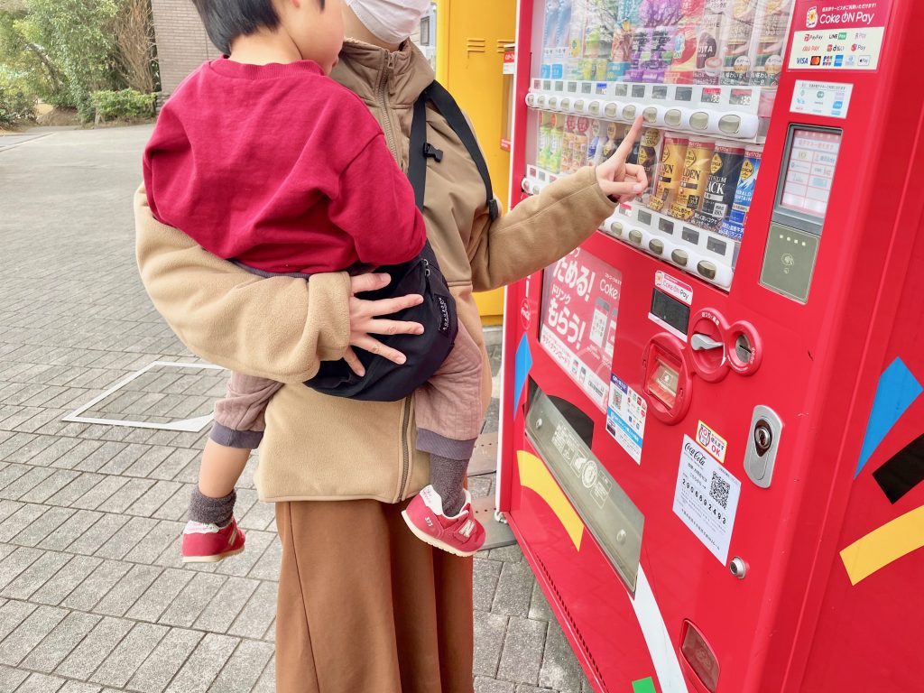 ボーンブーンで抱っこしながら自動販売機で飲み物を購入する写真